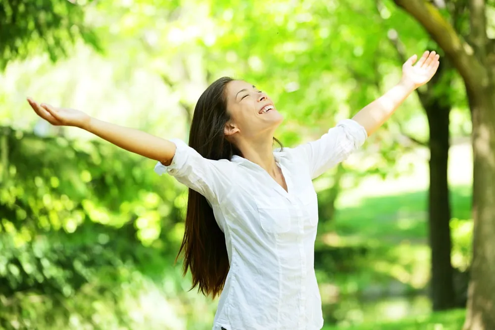 Femme souriante les bras ouverts dans la nature.